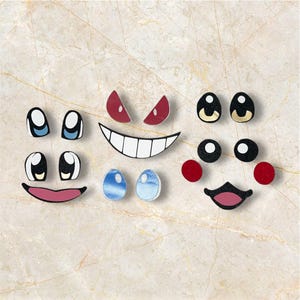 May include: A selection of cartoon face components, including eyes, mouths, and eyebrows, displayed on a light, patterned surface. The elements are in various colours, such as red, blue, black, and white.