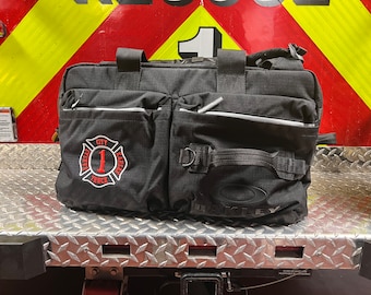Könnte beinhalten: Schwarze Reisetasche mit einem roten und weißen gestickten Aufnäher mit der Aufschrift "Kansas City Fire Truck 1". Die Tasche hat auch ein schwarzes Oakley-Logo auf der Vorderseite.