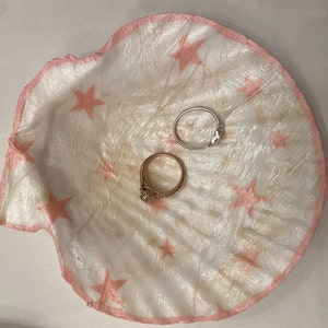 May include: A white ceramic dish with a pink, scalloped edge and a star pattern. Two rings are resting on the dish.