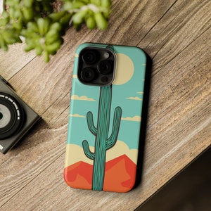 May include: A phone case with a retro-style illustration of a green cactus against a blue sky with white clouds. The case has a camera cutout and a white sun.