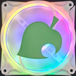 May include: A white computer fan with a green leaf design in the center. The fan's blades are visible through the center, and the outer ring glows with a rainbow of colors. The fan is square-shaped.