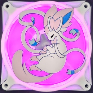 May include: A computer fan with a pink LED glow, featuring a cartoon character in white, pink, and blue. The fan has a square frame with rounded corners and a white border. The character is centered on the fan.
