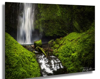 Könnte beinhalten: Ein Foto eines Wasserfalls, der eine Felswand hinunterfließt, umgeben von üppigem grünen Moos und Vegetation. Das Wasser speist einen kleinen Bach und schafft eine ruhige Naturlandschaft. Das Bild fängt die Schönheit der Natur ein.