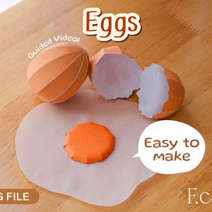 Op de afbeelding: Papieren eierschalen en een dooier op een lichtbruin oppervlak. Het woord "Eggs" staat bovenaan, met "Easy to make" in een tekstballon. De tekst "SVG FILE" staat onderaan.