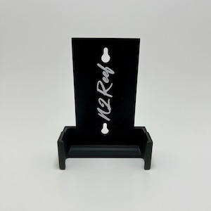 May include: Black wall mount with a white logo that says "M2 Reef". The mount has a slot for holding a phone or other device.