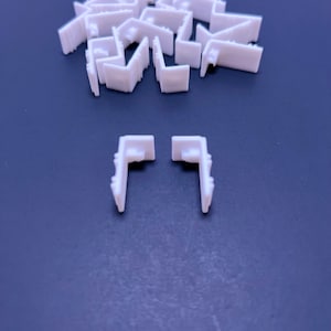 May include: A pile of white plastic corner brackets, with two additional brackets in the foreground.