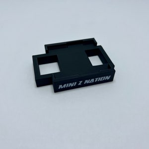 May include: Black plastic holder with two rectangular openings and the text "MINI Z NATION" printed on the front.