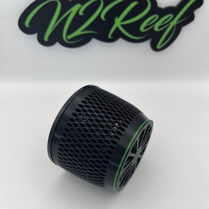 May include: Black cylindrical object with a lattice design and a green accent ring. The object is angled slightly, revealing its interior. The text "W2 Reef" is above the object in green script on a black background.
