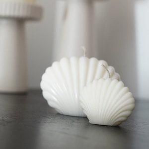 May include: Two white shell-shaped candles on a black surface. The candles are in front of two white candle holders with white candles.