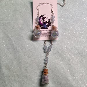 May include: Sterling silver necklace and earrings with blue glass bottles filled with crystals. The necklace has a pendant with a blue glass bottle filled with crystals. The earrings have blue glass bottles filled with crystals. The jewelry is made by Moon Violet Witchery.
