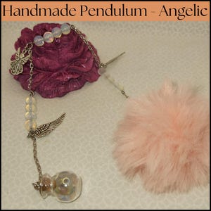 May include: A handmade pendulum with a pink fluffy pom-pom, a silver chain, and a glass bottle filled with iridescent glitter. The chain has a silver angel wing charm, a silver butterfly charm, and several white opal beads.