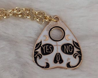 May include: A gold chain necklace with a white and black Ouija board pendant. The pendant features a skull design with the words "YES" and "NO" on either side.