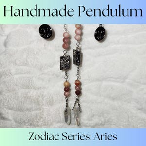 May include: Handmade pendulum with pink and brown beads, silver chains, and two clear crystal points. The pendulum has a silver charm with a textured design and the text "Zodiac Series: Aries".