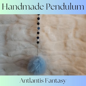 May include: A handmade pendulum with a blue pom-pom at the end. The pendulum is made with black, white, and blue beads and a silver chain. The text "Atlantis Fantasy" is at the bottom of the image.