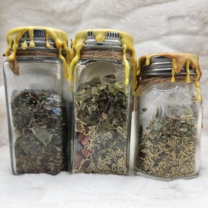 May include: Three glass jars with yellow wax seals and twine tied around the lids. Each jar contains a variety of dried herbs, crystals, and other natural ingredients.