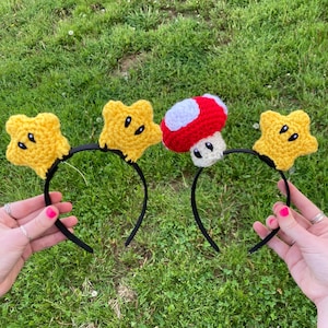 May include: Two black headbands with yellow star and red and white mushroom crochet embellishments.