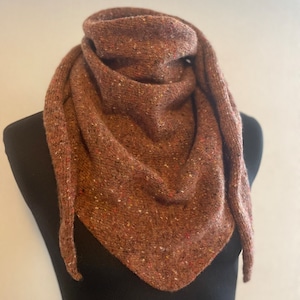 Puede incluir: Una bufanda de punto marrón con un patrón moteado. La bufanda está doblada y drapeada sobre un maniquí negro.