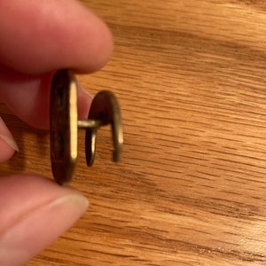 Puede incluir: Un bot&oacute;n de metal dorado con un dise&ntilde;o decorativo. El bot&oacute;n tiene un v&aacute;stago en la parte posterior para sujetarlo a la tela.