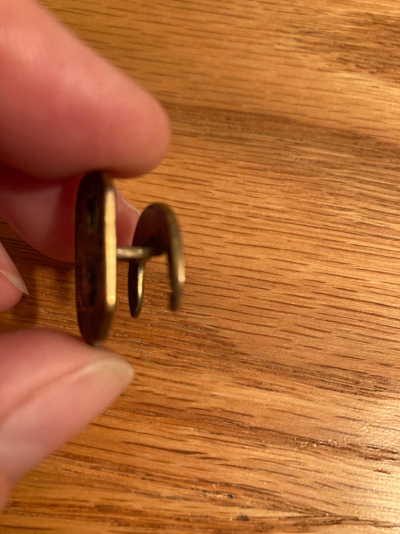 Puede incluir: Un bot&oacute;n de metal dorado con un dise&ntilde;o decorativo. El bot&oacute;n tiene un v&aacute;stago en la parte posterior para sujetarlo a la tela.