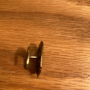 Puede incluir: Un bot&oacute;n de metal dorado con un dise&ntilde;o decorativo. El bot&oacute;n tiene un poste en la parte posterior para sujetarlo a la tela.