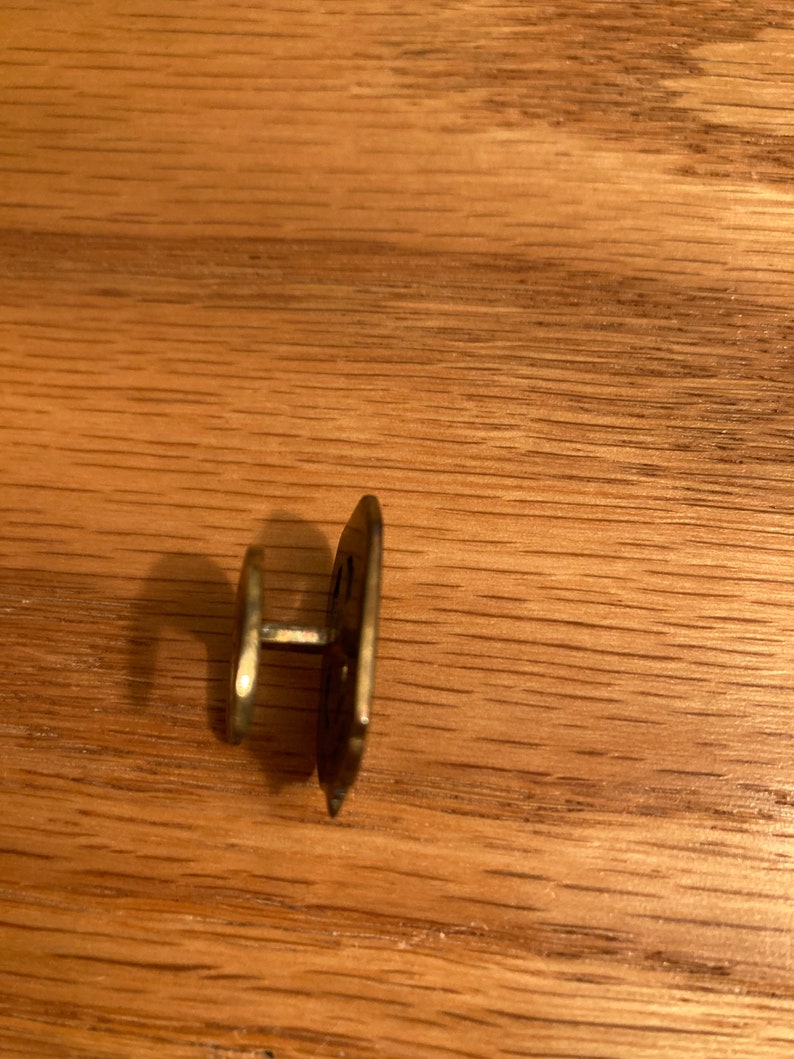 Puede incluir: Un bot&oacute;n de metal dorado con un dise&ntilde;o decorativo. El bot&oacute;n tiene un poste en la parte posterior para sujetarlo a la tela.