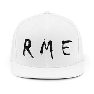 Puede incluir: Una gorra snapback blanca con el texto negro RME impreso en la parte frontal. La gorra tiene una corona estructurada, una visera plana y un botón en la parte superior central. El diseño es limpio y sencillo, destacando las letras negras.
