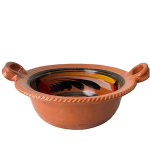 Könnte beinhalten: Eine handgefertigte Keramikschale in Terrakotta-Farbe mit zwei Griffen. Die Schale hat einen dekorativen Rand und ein bemaltes Innendesign mit schwarzen, roten, gelben und grünen floralen Mustern. Diese rustikale Schüssel eignet sich zum Servieren von Speisen.