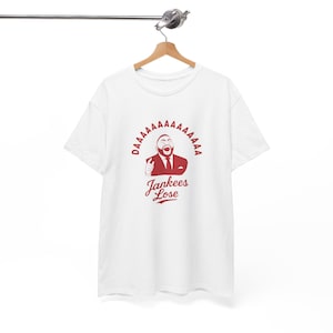 May include: White t-shirt with a red graphic. The graphic features a cartoon man in a suit with the text "DAAAAAAAA" around the top and "Jankees Lose" below. The man is making a peace sign.
