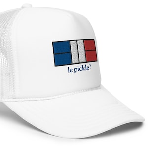 Könnte beinhalten: Weisse Trucker-Cap mit Mesh-Rückseite und gebogenem Schirm. Auf der Vorderseite befindet sich ein gesticktes Design der französischen Flagge und der Text "le pickle?" in Blau. Ein lässiges Accessoire.