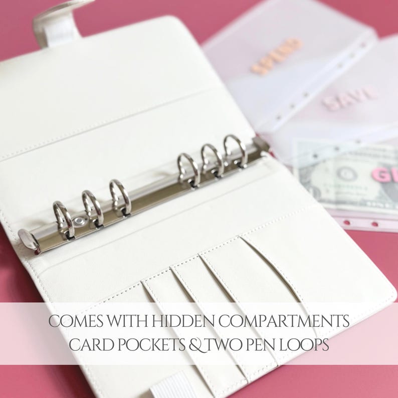 May include: Open white binder with silver rings, card pockets, and pen loops. The binder is open, revealing the interior with hidden compartments. The text on the image reads: COMES WITH HIDDEN COMPARTMENTS, CARD POCKETS & TWO PEN LOOPS.