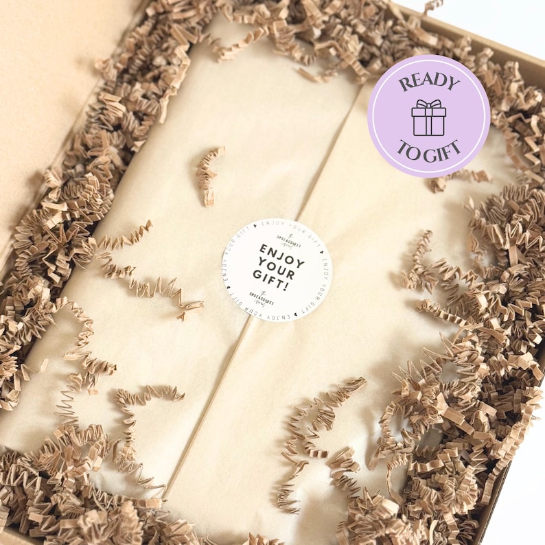 Puede incluir: Una caja de regalo de cart&oacute;n rellena de papel kraft arrugado, que contiene un paquete envuelto en papel de seda beige claro. Una pegatina circular en el papel dice ENJOY YOUR GIFT y una insignia circular morada dice READY TO GIFT.