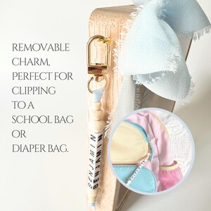 May include: A personalized keychain featuring natural wooden beads and white letter beads spelling the name BENJAMIN, attached to a gold-tone metal lobster clasp. A light blue frayed ribbon is tied to the top. A circular inset shows a similar keychain.