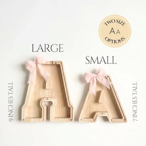 Puede incluir: Dos huchas de madera clara con forma de letra A, con frente transparente y lazos de tela rosa. La letra grande est&aacute; etiquetada como 9 INCHES TALL y la peque&ntilde;a como 7 INCHES TALL. El texto TWO SIZE OPTIONS aparece en una insignia circular.