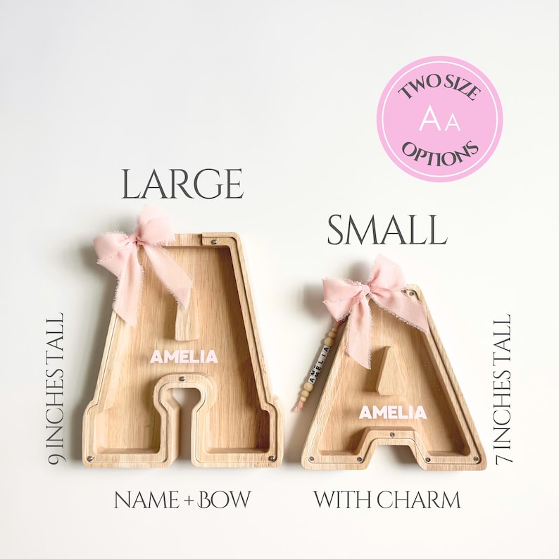 May include: Two wooden letter A piggy banks labeled LARGE and SMALL. The large bank is 9 inches tall with a pink bow. The small bank is 7 inches tall with a pink bow and a name charm. Both feature the name AMELIA printed in white on the front.
