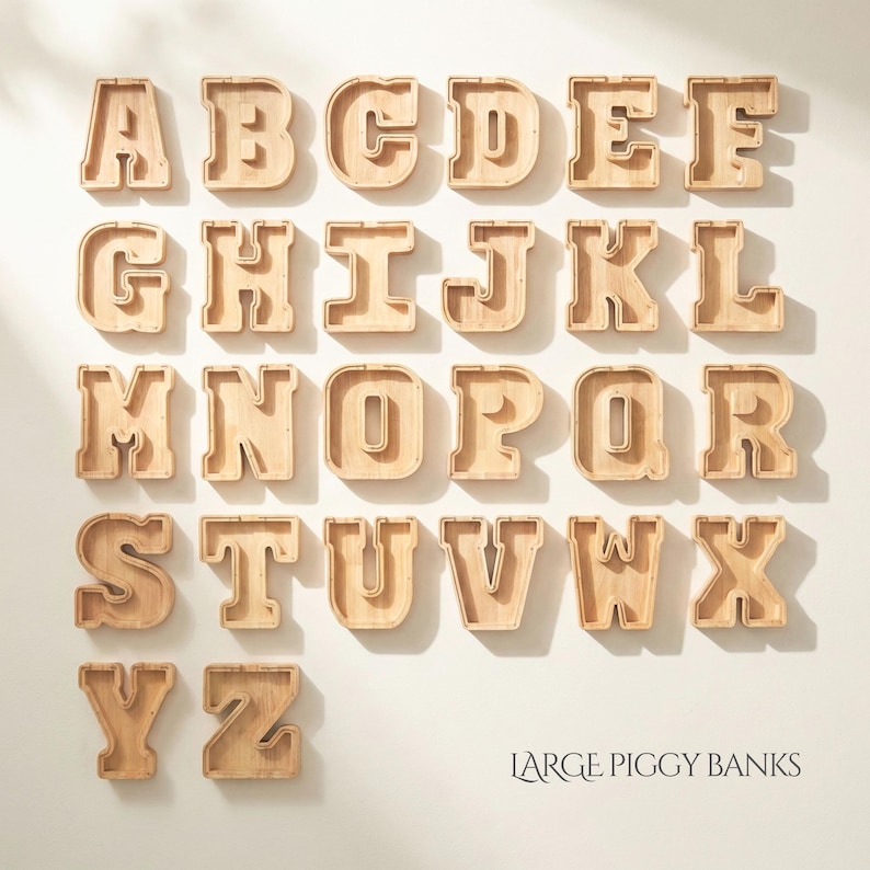 May include: A collection of twenty-six wooden letter-shaped piggy banks arranged in alphabetical order from A to Z. Each light-colored wooden letter features a hollow center and a clear front panel. The text LARGE PIGGY BANKS is printed in the bottom right.