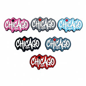 Può includere: Una collezione di sette accessori a tema Chicago in vari colori. Ogni accessorio presenta la parola "Chicago" in un font in stile graffiti, con un accento a stella. I colori includono rosa, grigio, blu, nero e rosso.