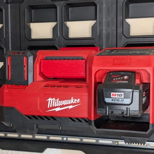 May include: Red Milwaukee power tool battery charger with a black M18 XC6.0 battery inserted. The charger is mounted on a black storage system. The Milwaukee logo is visible.