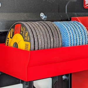May include: Red plastic storage organiser with two rows of abrasive discs. The top row has brown discs and the bottom row has blue discs. The organiser is attached to a black tool box.