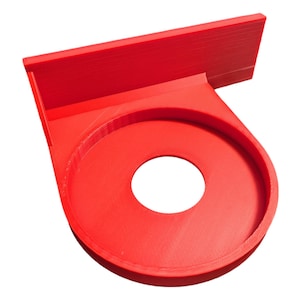 May include: A red plastic wall mount with a circular opening. The mount is designed to hold a round object, such as a roll of paper towels.