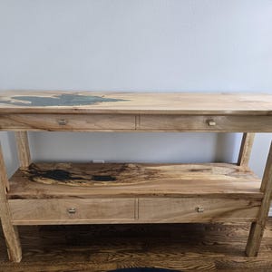 K&ouml;nnte beinhalten: Ein Holzkonsolentisch mit einer naturbelassenen Kante und einer dunklen Harzeinlage, zwei oberen Schubladen mit kleinen silberfarbenen Griffen sowie einem unteren Regal mit passender Harzeinlage und zwei weiteren Schubladen darunter.