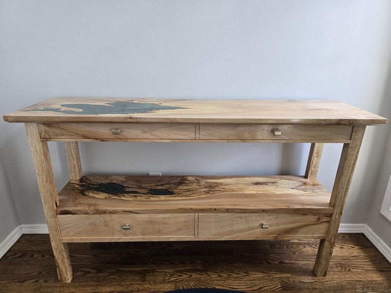 K&ouml;nnte beinhalten: Ein Holzkonsolentisch mit einer naturbelassenen Kante und einer dunklen Harzeinlage, zwei oberen Schubladen mit kleinen silberfarbenen Griffen sowie einem unteren Regal mit passender Harzeinlage und zwei weiteren Schubladen darunter.