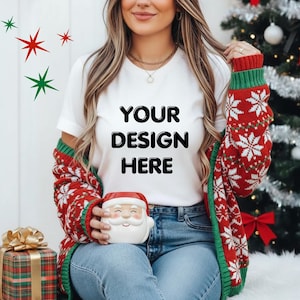 Könnte beinhalten: Ein weißes T-Shirt mit dem Text "YOUR DESIGN HERE" wird mit einer rot-weiß gemusterten Schneeflocken-Strickjacke getragen. Die Person hält einen Weihnachtsmann-Becher. Eine verpackte Geschenkbox mit goldener Schleife befindet sich links.
