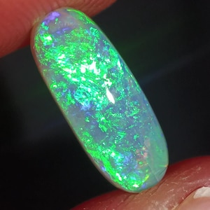 Peut inclure: Une pierre précieuse d'opale verte et blanche avec un éclat nacré. L'opale est de forme ovale et présente un éclat iridescent vert et bleu.