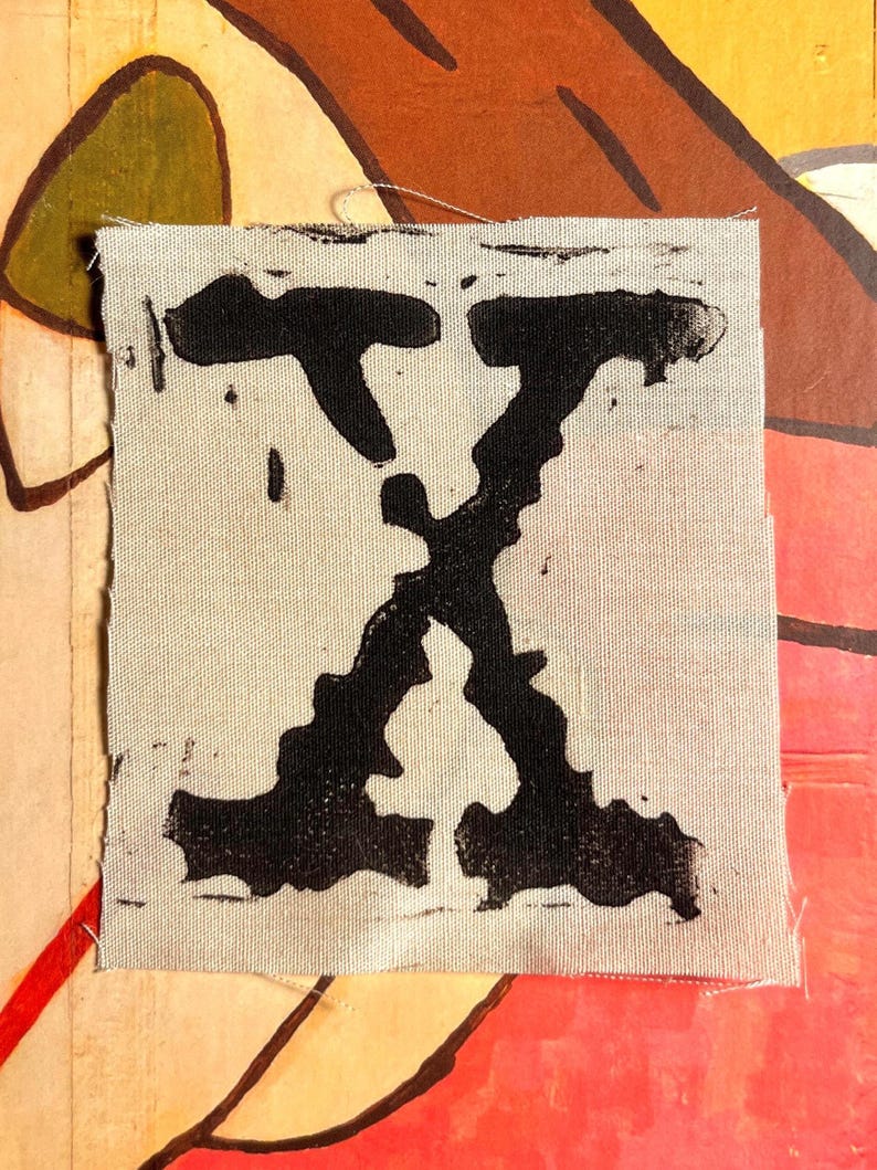 Peut inclure: Un patch de tissu carr&eacute; blanc cass&eacute; avec un grand "X" noir imprim&eacute;. Le "X" est stylis&eacute; avec des lignes &eacute;paisses et irr&eacute;guli&egrave;res, donnant un aspect imprim&eacute; &agrave; la main ou en bloc. Le fond est un collage color&eacute;.