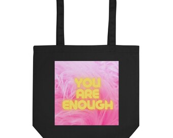Może przedstawiać: Czarna torba typu tote z różowo-żółtym wzorem. Wzór zawiera napis "YOU ARE ENOUGH" w kolorze żółtym.