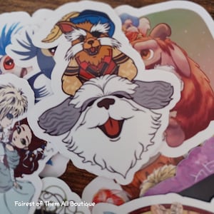 May include: A collection of colorful stickers featuring cartoon characters. The stickers include a smiling white dog with gray ears, a raccoon-like character in a red vest, and other animated figures. The stickers are on a wooden surface.