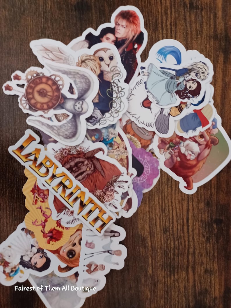 May include: A collection of colorful stickers featuring characters and imagery from the movie "Labyrinth." The stickers include images of David Bowie, owls, and other fantasy elements. The word "LABYRINTH" is printed in gold letters.