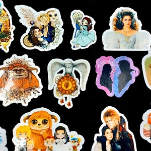 May include: A collection of colorful stickers featuring characters and scenes from the movie Labyrinth. The stickers include images of Jareth the Goblin King, Sarah, Hoggle, and other iconic characters. The stickers are on a black background.