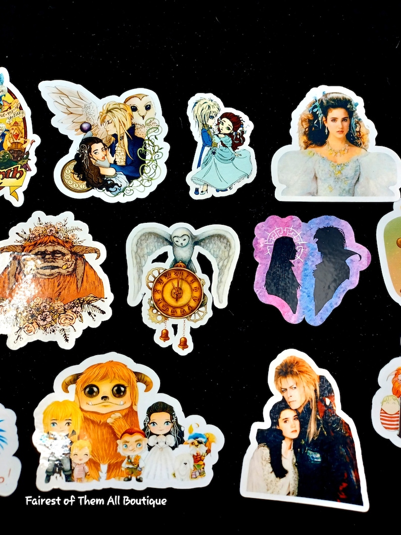 May include: A collection of colorful stickers featuring characters and scenes from the movie Labyrinth. The stickers include images of Jareth the Goblin King, Sarah, Hoggle, and other iconic characters. The stickers are on a black background.