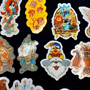 May include: A collection of colorful stickers featuring characters and scenes from the movie Labyrinth. The stickers include images of goblins, the Fireys, and other fantasy creatures. The stickers are on a black background.